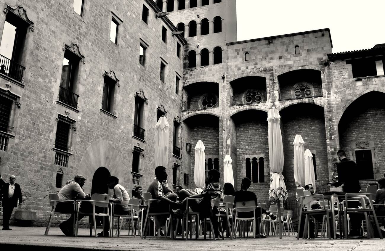 Tische und Sonnenschirme unter dem gotischen Gemäuer der Plaça del Rei