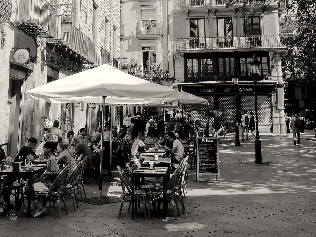 Belebte Caféterrasse im Gotischen Viertel, Sonnenschirm aufgespannt, Gäste im Gespräch beim Mittagessen